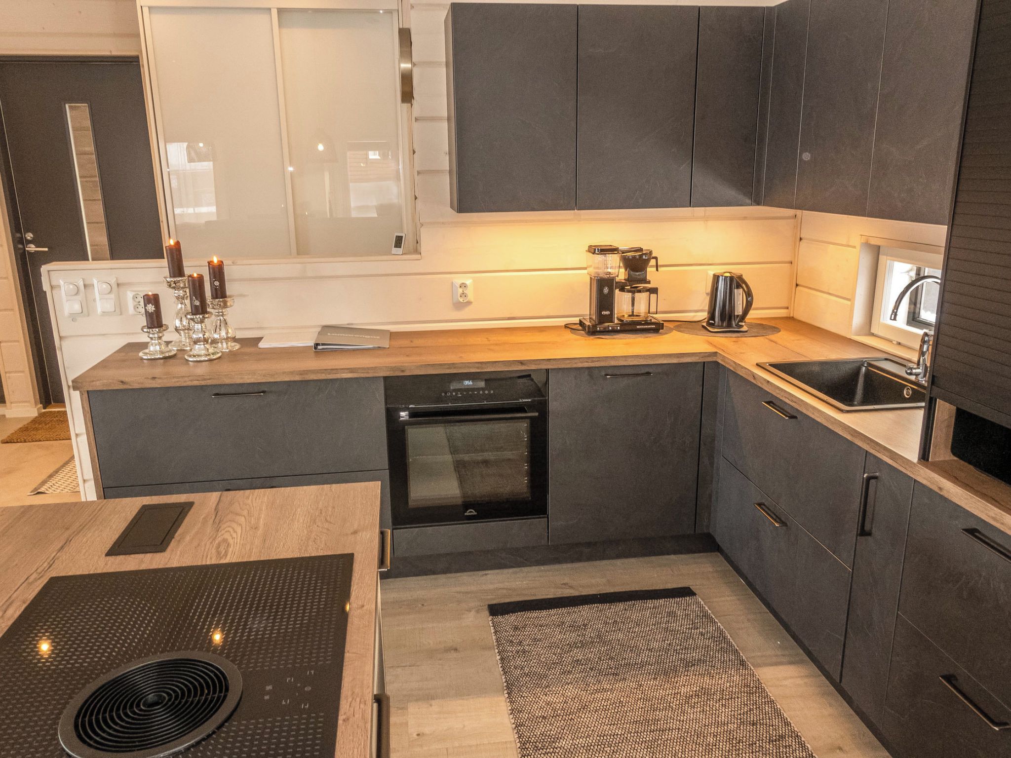 Una cucina moderna con mobili scuri, forno integrato, macchina da caffè e lavello.