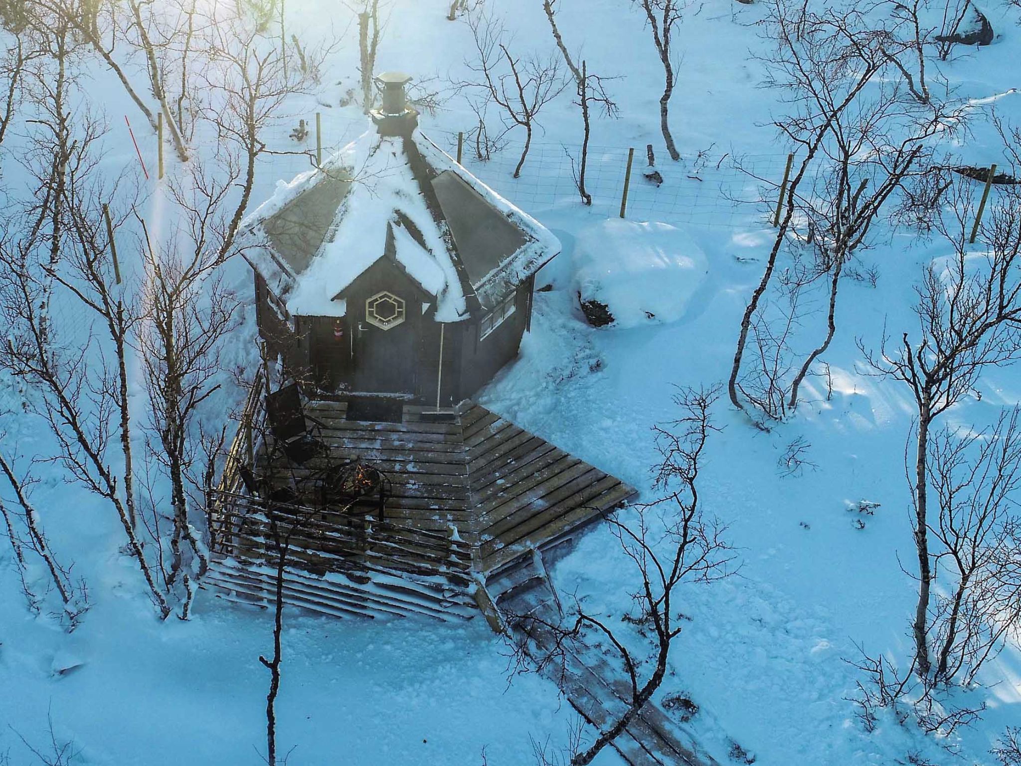A wooden structure with a snow-covered roof, surrounded by snow and leafless trees.