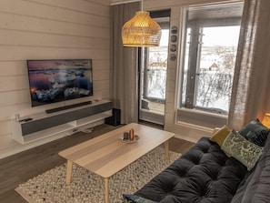Una sala de estar moderna con un televisor de pantalla plana, un sofá, una mesa de centro y un ventanal con vistas a un paisaje nevado.