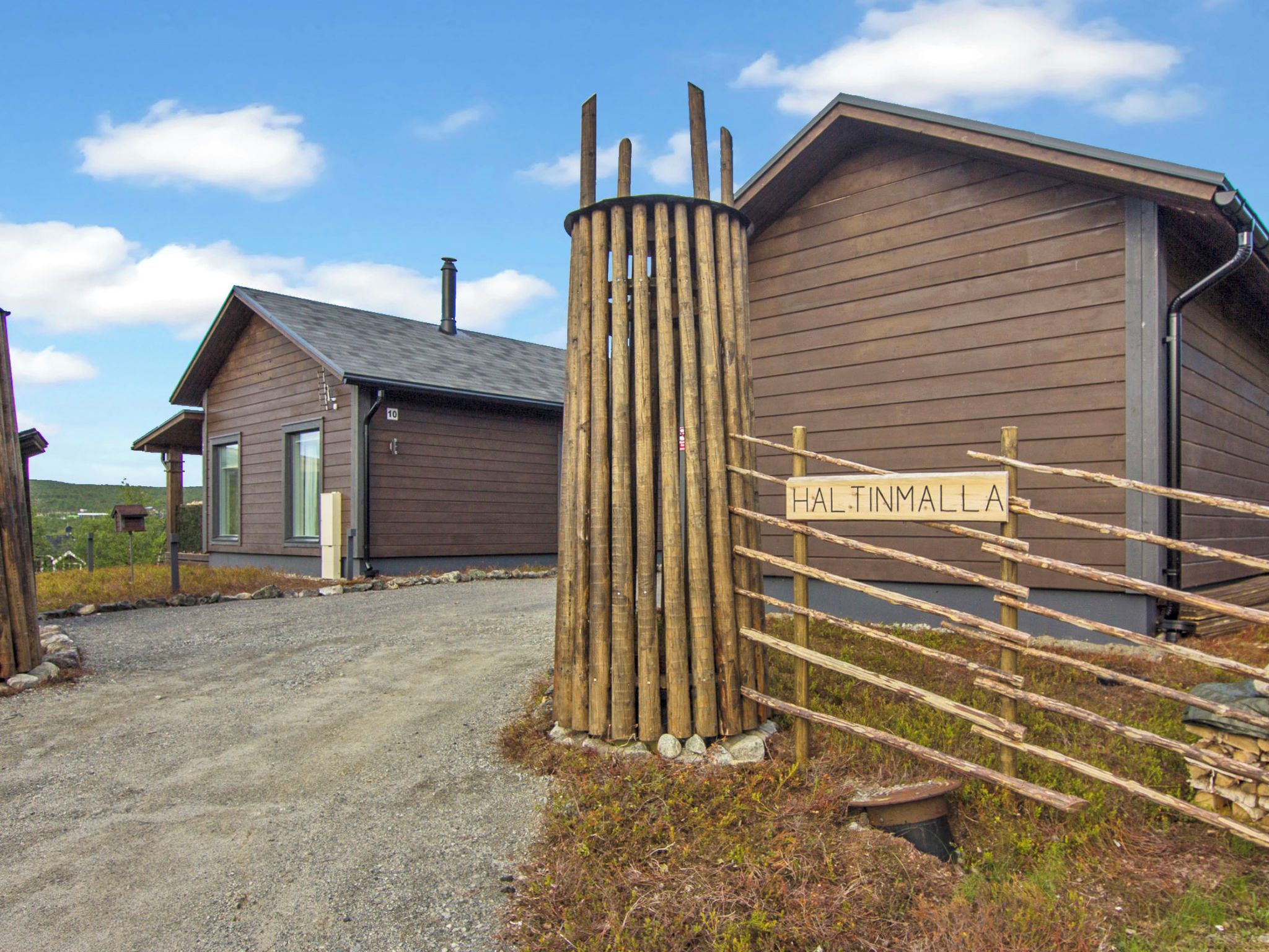A rustic wooden building with a sign reading 'HALTINMALLA' and a gravel driveway leading to it.