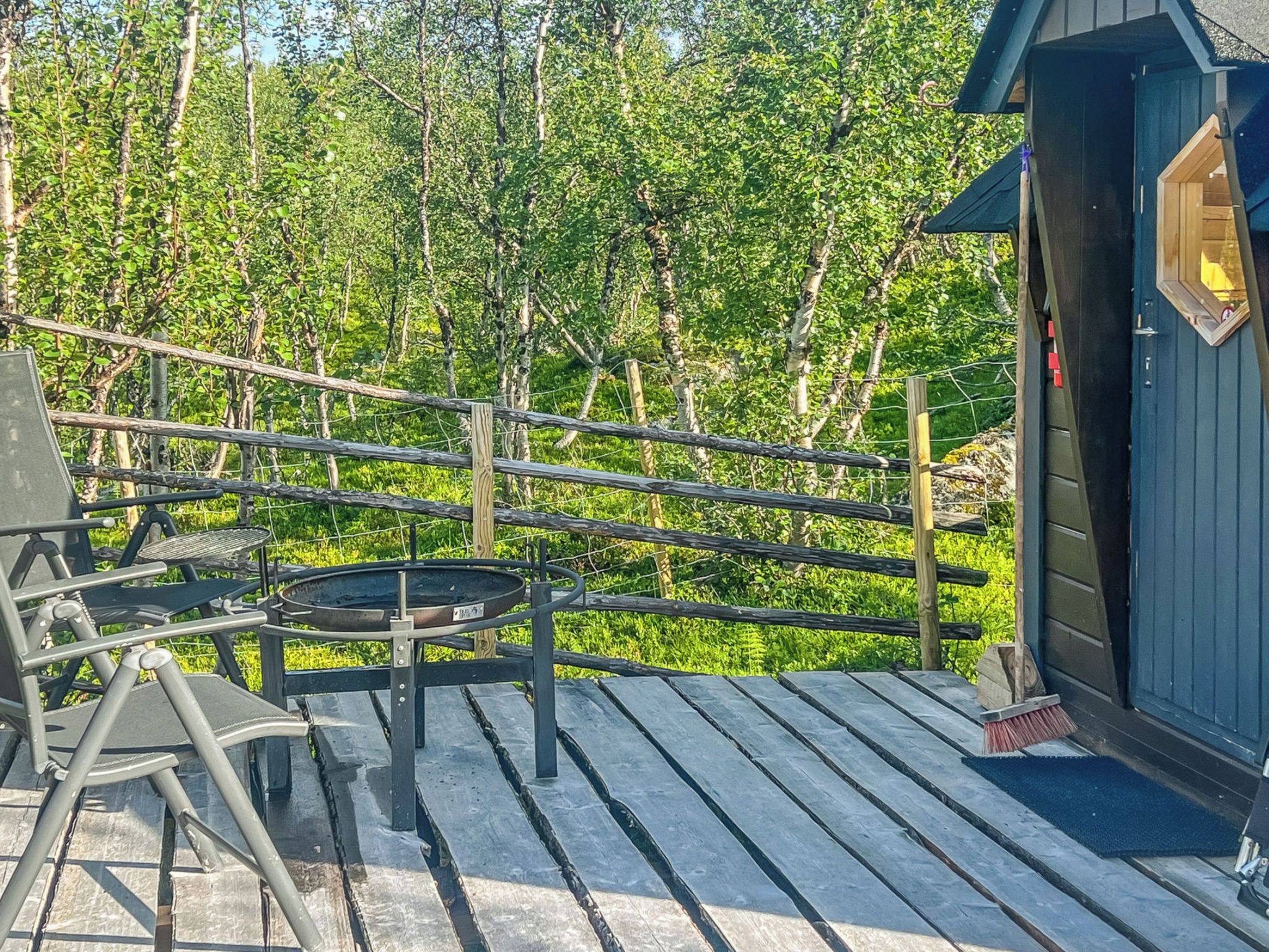 Une terrasse en bois avec une table et des chaises, un petit abri de jardin et un paysage boisé en arrière-plan.