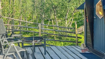 Eine Holzterrasse mit Tisch und Stühlen, eine kleine Gartenhütte und ein bewaldeter Hintergrund.
