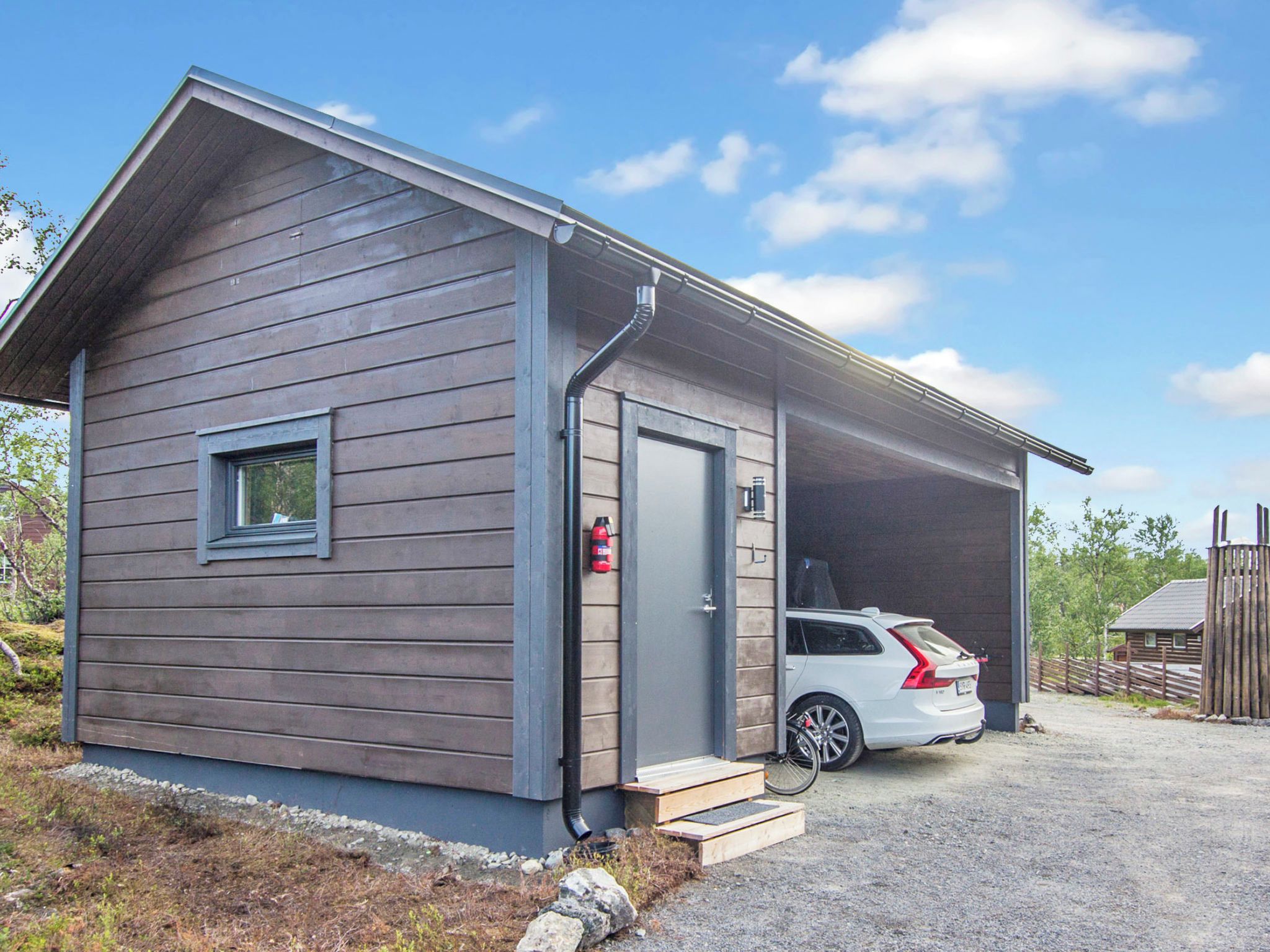 A small, single-story building with a covered parking area, a fire extinguisher mounted on the wall, and a vehicle parked inside.