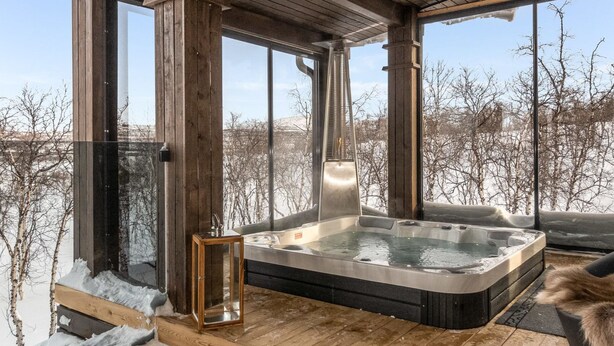 Een houten chalet met een hottub en grote ramen met uitzicht op een besneeuwd landschap.