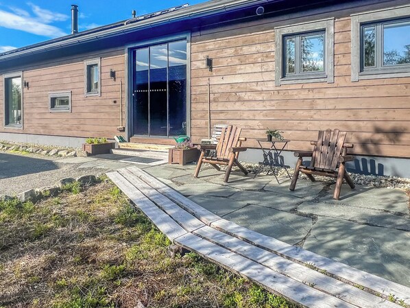 Ein modernes Gebäude mit Holzfassade, großen Schiebeglastüren und einer Terrasse mit Gartenmöbeln.