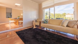 A modern living room with a large window, a sofa, a coffee table, and a dining area. - Mar Roig by Interhome (L'Ampolla)