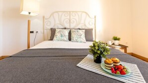 A neatly made bed with a grey bedspread, a white headboard, and two pillows. There is a small table with a plant and a plate of food. - Mar Roig by Interhome (L'Ampolla)