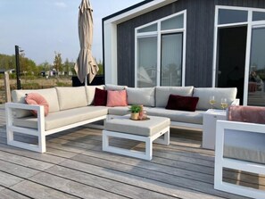 A modern outdoor living area with a sofa, ottoman, and chairs, a table with drinks, and a large umbrella.