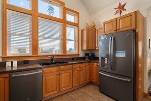 A kitchen with wooden cabinets, a stainless steel refrigerator, and a window with blinds. - Soundbreeze Sunset: Golf and sound views, hot tub, dog friendly, elevator. (Nags Head)