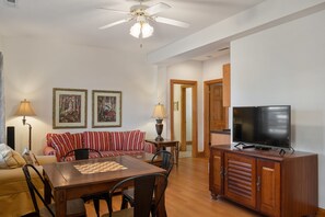 A living room with a sofa, a dining table with chairs, a television on a wooden cabinet, and two lamps. - Soundbreeze Sunset: Golf and sound views, hot tub, dog friendly, elevator. (Nags Head)