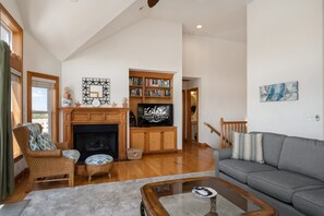 A spacious living room with a fireplace, a bookshelf, a television, and a sofa. - Soundbreeze Sunset: Golf and sound views, hot tub, dog friendly, elevator. (Nags Head)