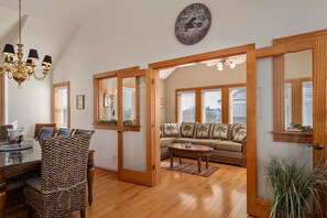 A spacious living room with a wooden floor, a sofa, a coffee table, and a chandelier. - Soundbreeze Sunset: Golf and sound views, hot tub, dog friendly, elevator. (Nags Head)