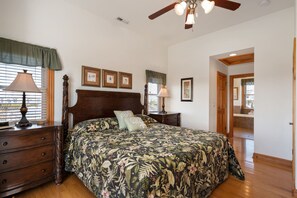 A bedroom with a large bed, wooden headboard, two bedside tables with lamps, a dresser, and framed pictures on the wall. - Soundbreeze Sunset: Golf and sound views, hot tub, dog friendly, elevator. (Nags Head)