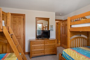 A bedroom with bunk beds, a dresser, a TV, and wooden furniture. - Soundbreeze Sunset: Golf and sound views, hot tub, dog friendly, elevator. (Nags Head)