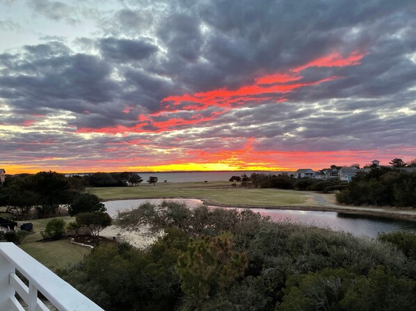 A sunset over a residential area with a body of water, trees, and houses. - Soundbreeze Sunset: Golf and sound views, hot tub, dog friendly, elevator. (Nags Head)