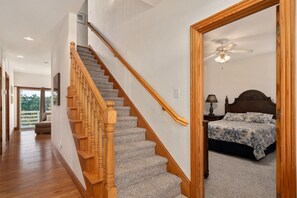 A staircase with wooden balusters leading to a bedroom with a bed and a nightstand. - Soundbreeze Sunset: Golf and sound views, hot tub, dog friendly, elevator. (Nags Head)