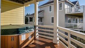 Una terraza de madera con un jacuzzi, barandillas blancas y una casa al fondo.