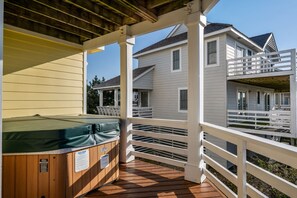A wooden deck with a hot tub, white railings, and a house in the background.