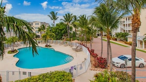 Une piscine à bord incurvé, entourée de palmiers et d’une clôture blanche.