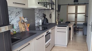 Una cocina compacta con encimera negra, armarios blancos y horno empotrado. Se observa un pequeño comedor con una mesa y sillas a través de una puerta abierta.