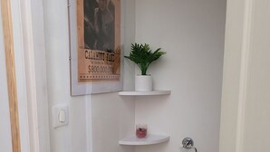 Un baño pequeño con un cartel que dice 'WANTED', una planta en maceta, un dispensador de papel higiénico y una pequeña repisa con una vela.