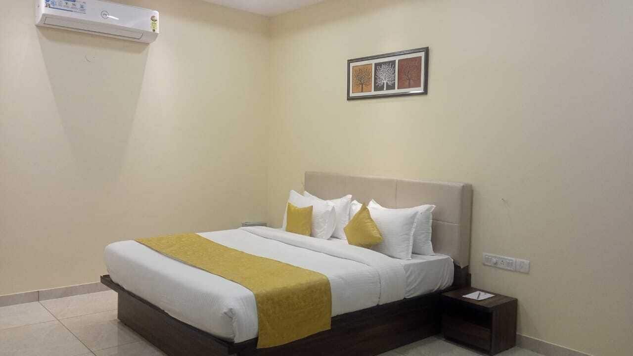 A neatly made bed with a white and yellow bedspread, a headboard, and a nightstand with a lamp.