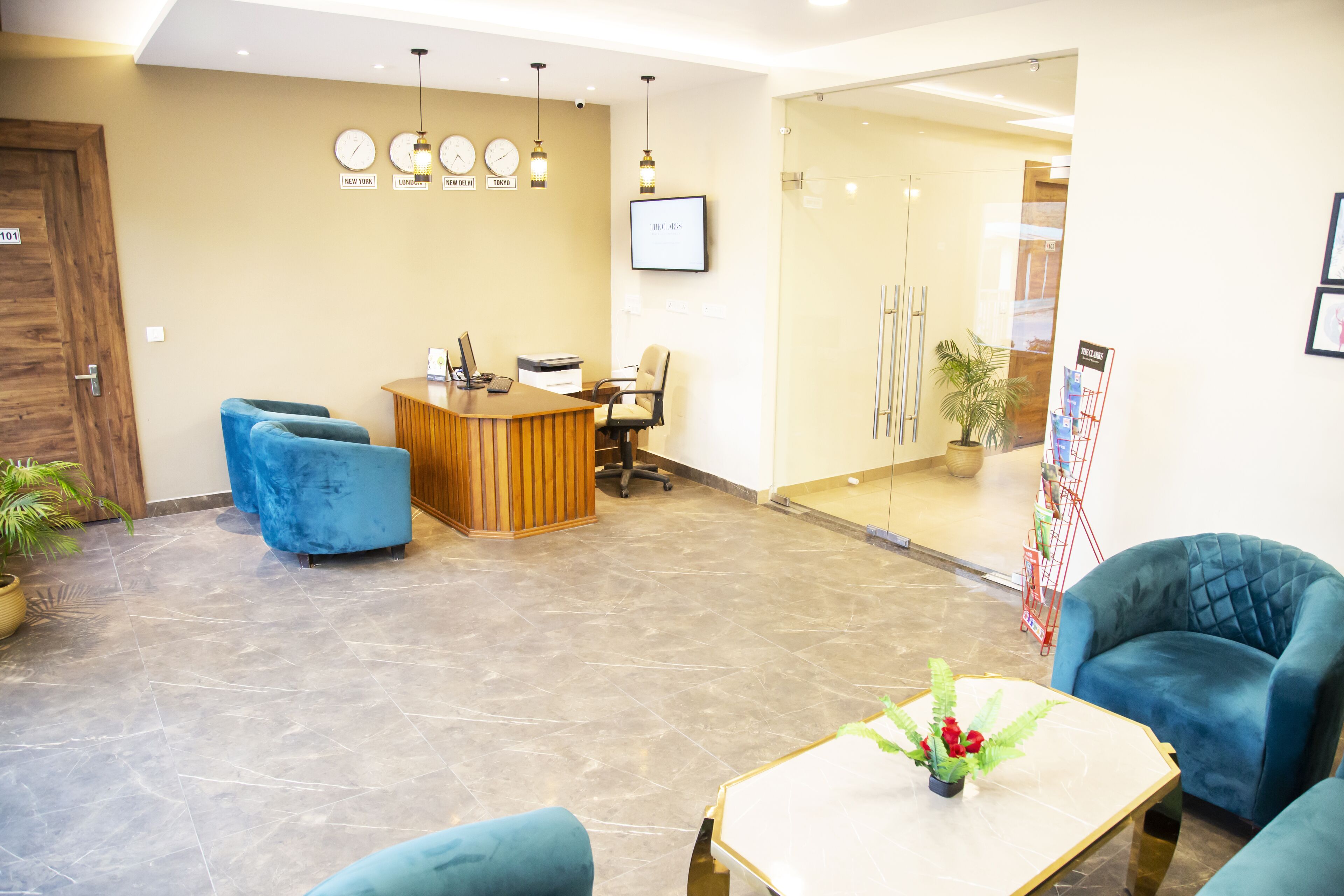 A reception area with a wooden desk, blue chairs, a clock, and a potted plant.
