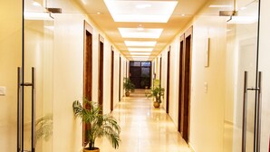 A hotel corridor with glass doors, potted plants, and a tiled floor.