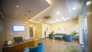 A modern reception area with a wooden desk, blue seating, and a flat-screen TV displaying 'THE CLARKS'.