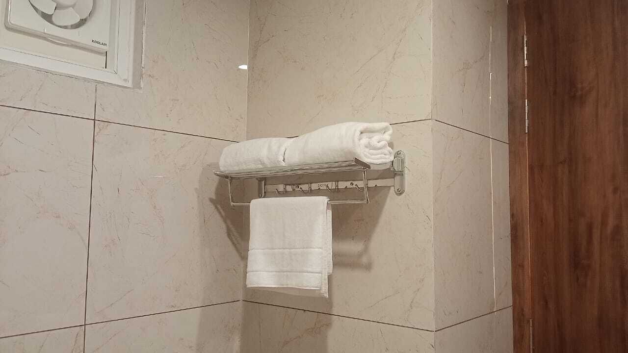 Un baño con piso de mármol, un perchero con dos toallas y un dispensador de toallas en la pared.