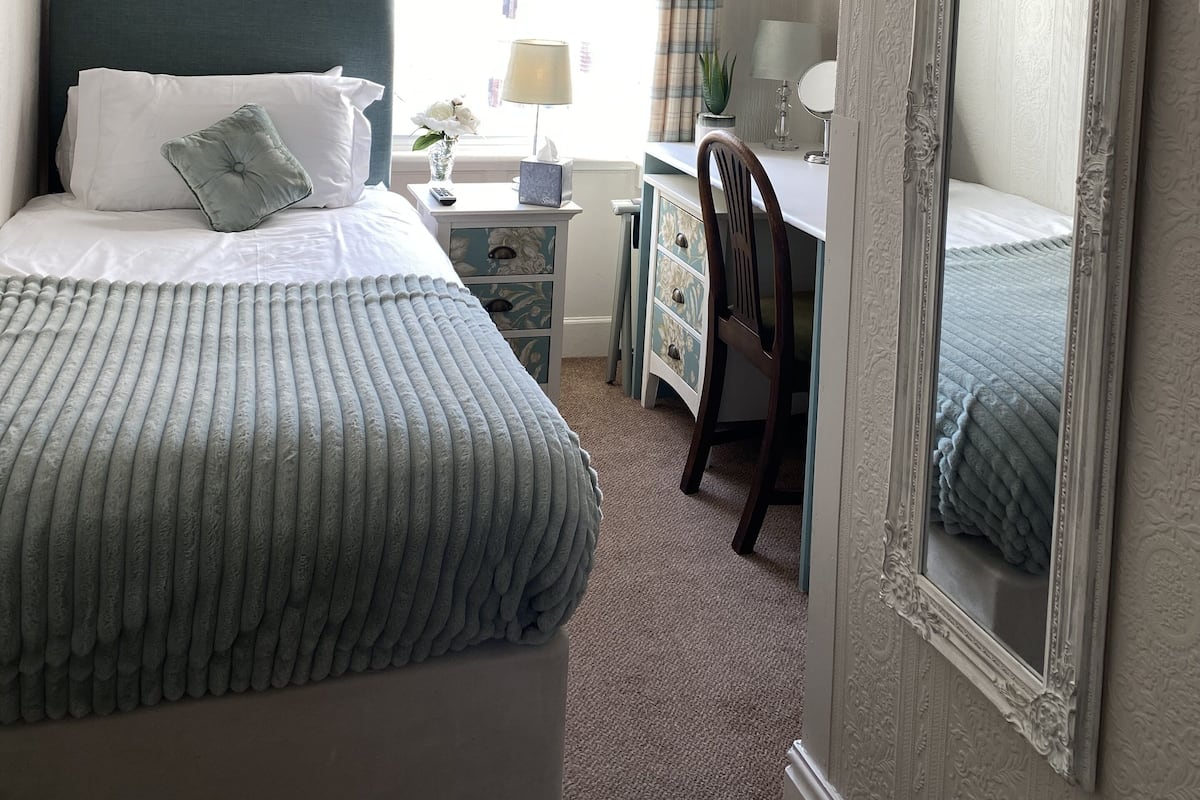 A bedroom with a bed, a desk, a chair, a mirror, and a window with curtains.