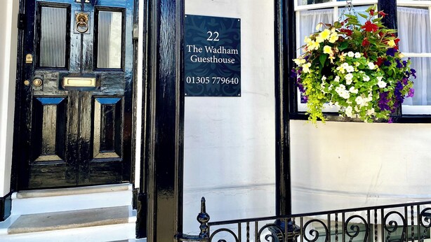A black door with the number 22, a sign for The Wadham Guesthouse, and a hanging flower basket. - The Wadham (Weymouth)