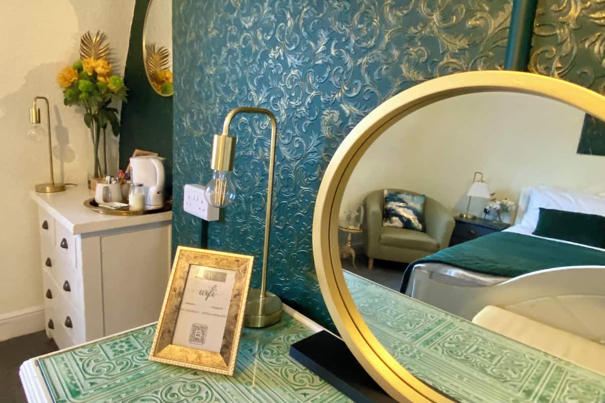 A hotel room with a bed, a bedside table with a lamp, a dresser, and a mirror.