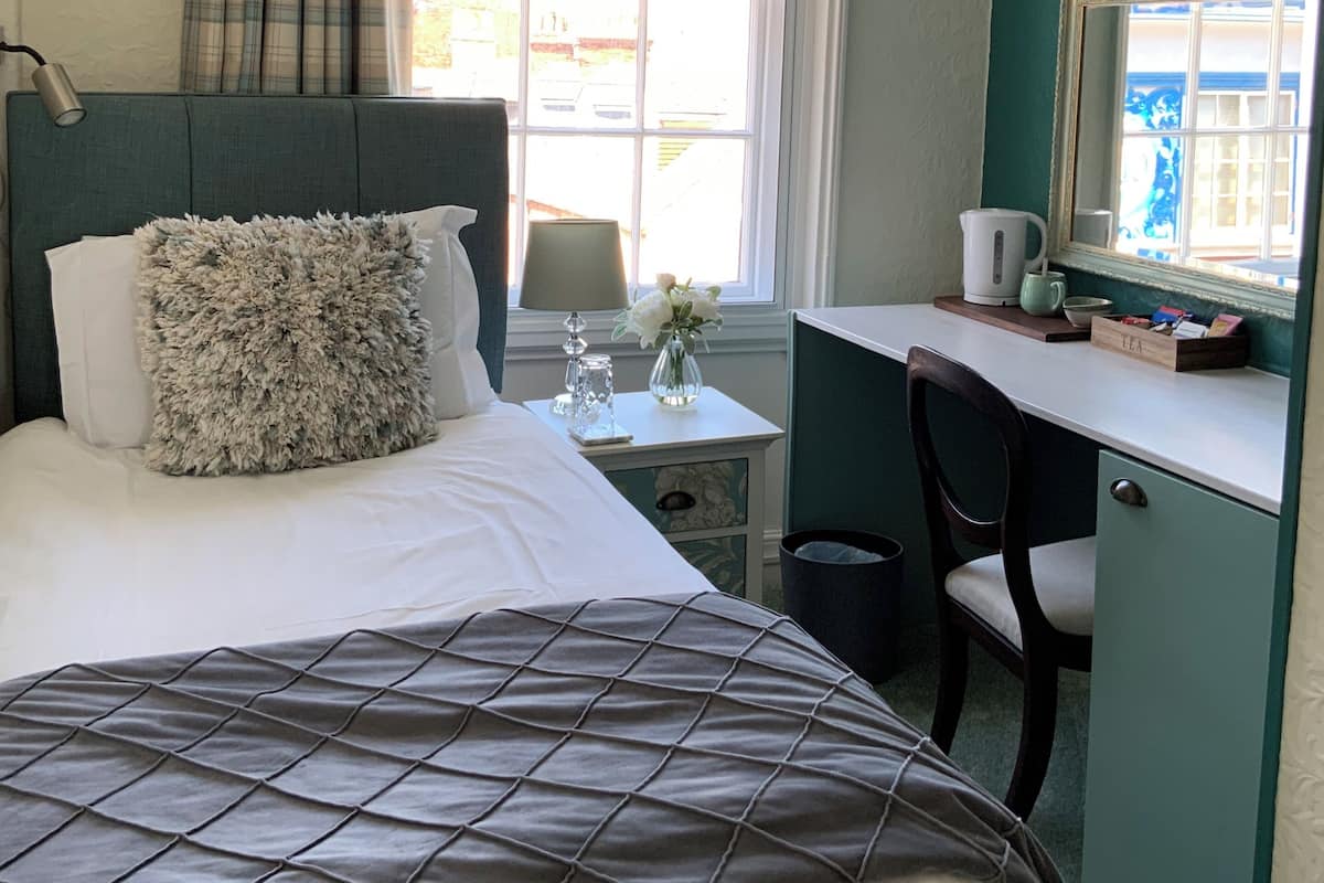 A hotel room with a bed, a desk, a chair, a window, and a chandelier.