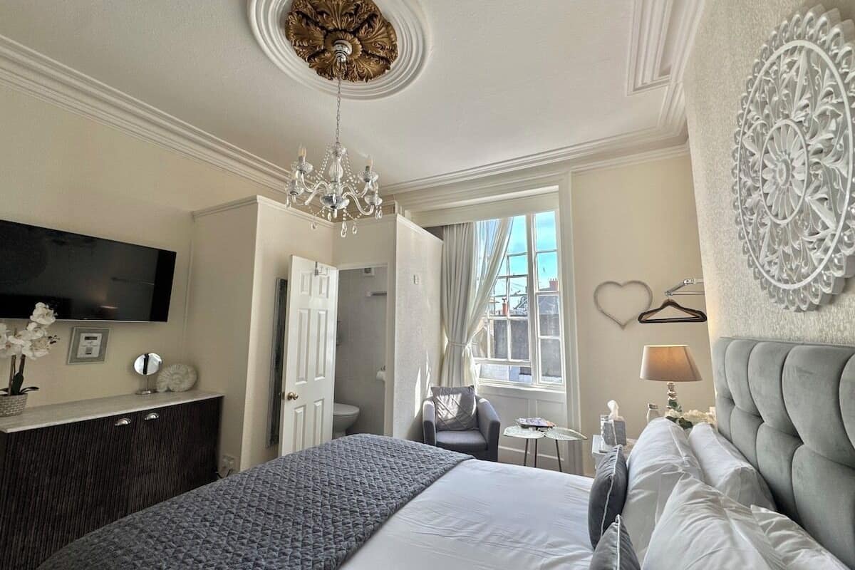 A hotel room with a large bed, a television mounted on the wall, a chandelier, and a decorative wall piece.