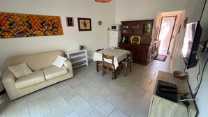 A living room with a sofa, a dining table, and a kitchen area with cabinets and a TV. - Pinus Village 170m from the beach (Santa Margherita di Pula)
