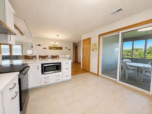 A modern kitchen with white cabinets, a microwave, and a dining area with a table and chairs. - Our Legacy - Dog Friendly Oceanside 4 BR Cottage with Community Pool access (Duck)