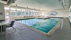 An indoor swimming pool with clear water, sunlit by large windows, and a logo on the wall. - Our Legacy - Dog Friendly Oceanside 4 BR Cottage with Community Pool access (Duck)