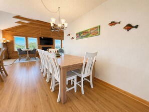 A dining area with a wooden table and chairs, a chandelier, and a view of the outdoors.