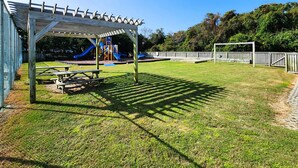 A covered picnic area with benches, a playground with slides, and a fenced play area. - Our Legacy - Dog Friendly Oceanside 4 BR Cottage with Community Pool access (Duck)