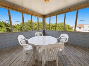 A covered outdoor area with a round table and four chairs, surrounded by large windows.