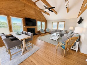 A spacious living room with a wooden ceiling, a fireplace, a television, and a dining area with a table and chairs.