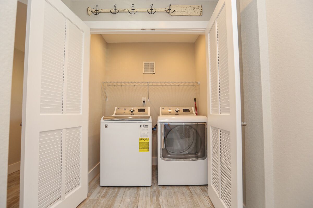 A laundry room with two white washers and dryers, a clothesline, and a vented ceiling.
