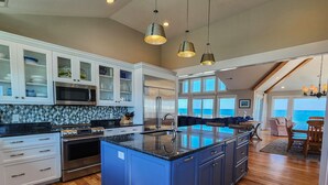 Een moderne keuken met een groot eiland, roestvrijstalen apparatuur en uitzicht naar buiten.