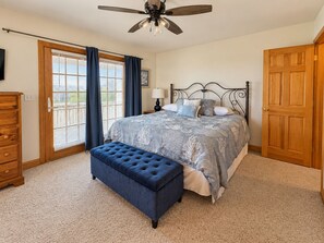 A bedroom with a bed, a bench, a ceiling fan, a door, and a window with curtains.