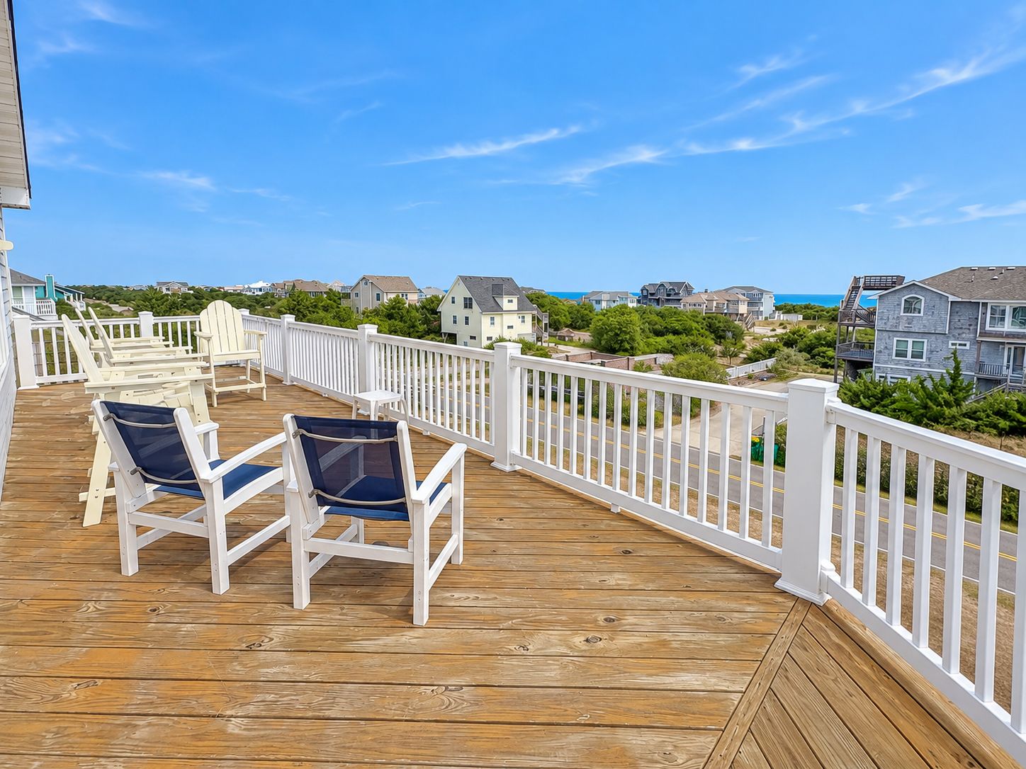 A wooden deck with two chairs and a small table, overlooking a residential area with houses and a clear sky.