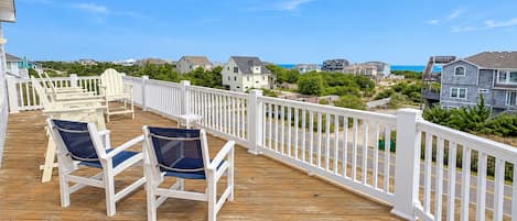A wooden deck with two chairs and a small table, overlooking a residential area with houses and a clear sky.
