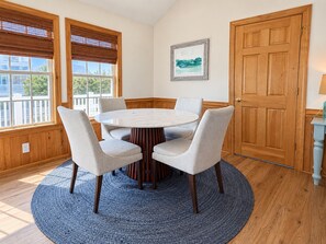 Una habitación con una mesa redonda rodeada por cuatro sillas, una puerta de madera y una ventana con persianas.