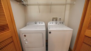 A laundry room with two white front-loading washing machines and a shelf above them.