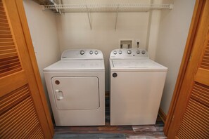 A laundry room with two white front-loading washing machines and a shelf above them.
